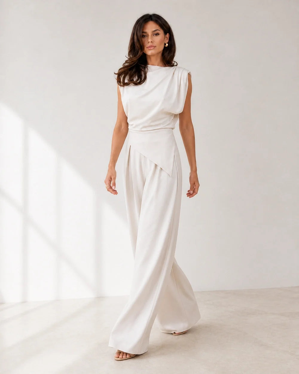 Women's white asymmetric draped top and wide-leg trousers set, walking view.